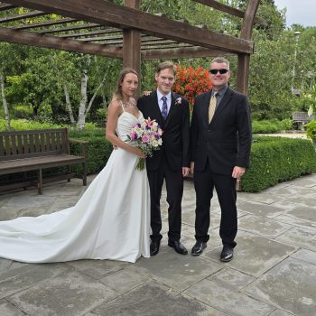 Bride and groom standing outdoors with their wedding officiant