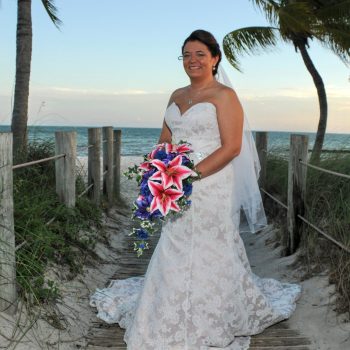 Bride posing in her wedding dress beside a tropical beach